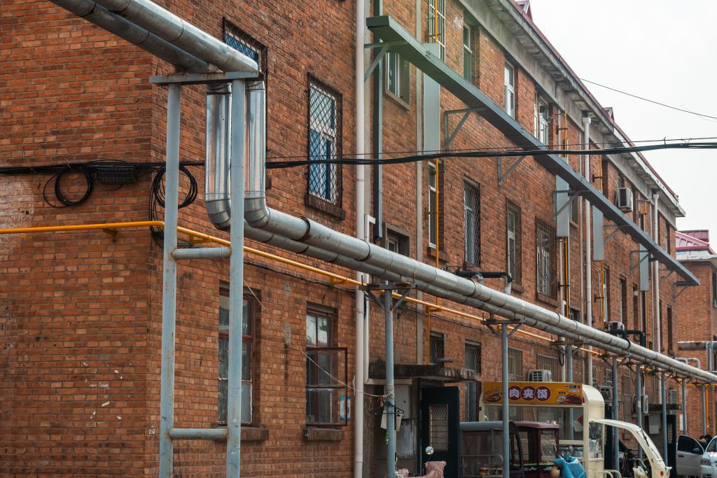 Exterior view of brick building with exposed industrial pipes and utility lines.